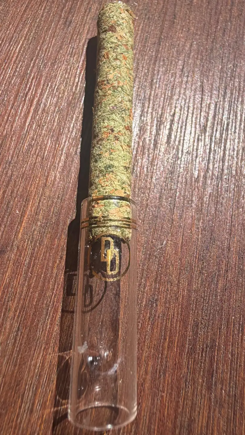 Full-length PURE paperless preroll prototype with a clear custom glass tip and gold DD Signature bands on a wooden table